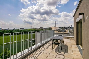 A balcony with a view of a sports field, a table and chairs, and a building with a modern design. - Sunlit Landstraße 1BR w/ Elevator & Playglound, Calm Area, by Blueground (Vienna)