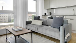 A modern living room with a grey sofa, a small wooden table, and a kitchen area with white cabinets and a stainless steel range hood. - Sunlit Landstraße 1BR w/ Elevator & Playglound, Calm Area, by Blueground (Vienna)