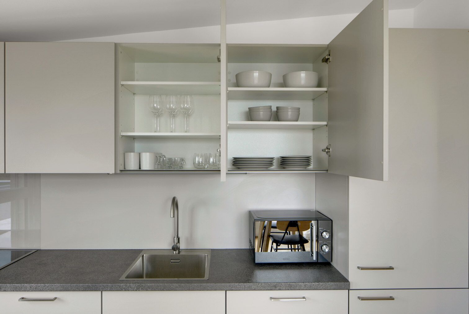 Een moderne keuken met een inbouwspoelbak, een broodrooster en open planken met servies en glazen.