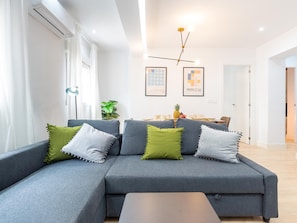 A modern living room with a grey sectional sofa, green and white pillows, a coffee table, a plant, and artwork on the wall.