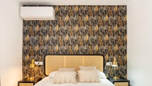 Un lit bien fait, avec une couette blanche, une tête de lit à motifs tissés et un mur orné d’un motif végétal.