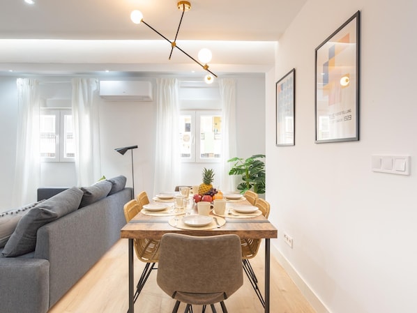 A modern dining area with a wooden table, wicker chairs, and a grey sofa.