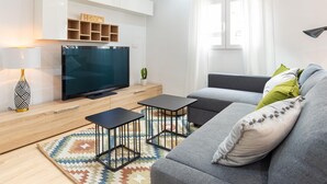 Un salon moderne avec un téléviseur à écran plat, un canapé, deux tables d’appoint, un tapis à motifs et une plante en pot.