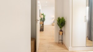 Un couloir avec un plancher en bois, une plante en pot et un miroir accroché au mur.