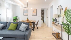 Un salon moderne avec un canapé gris, une table à manger avec des chaises et, au fond, un coin cuisine.