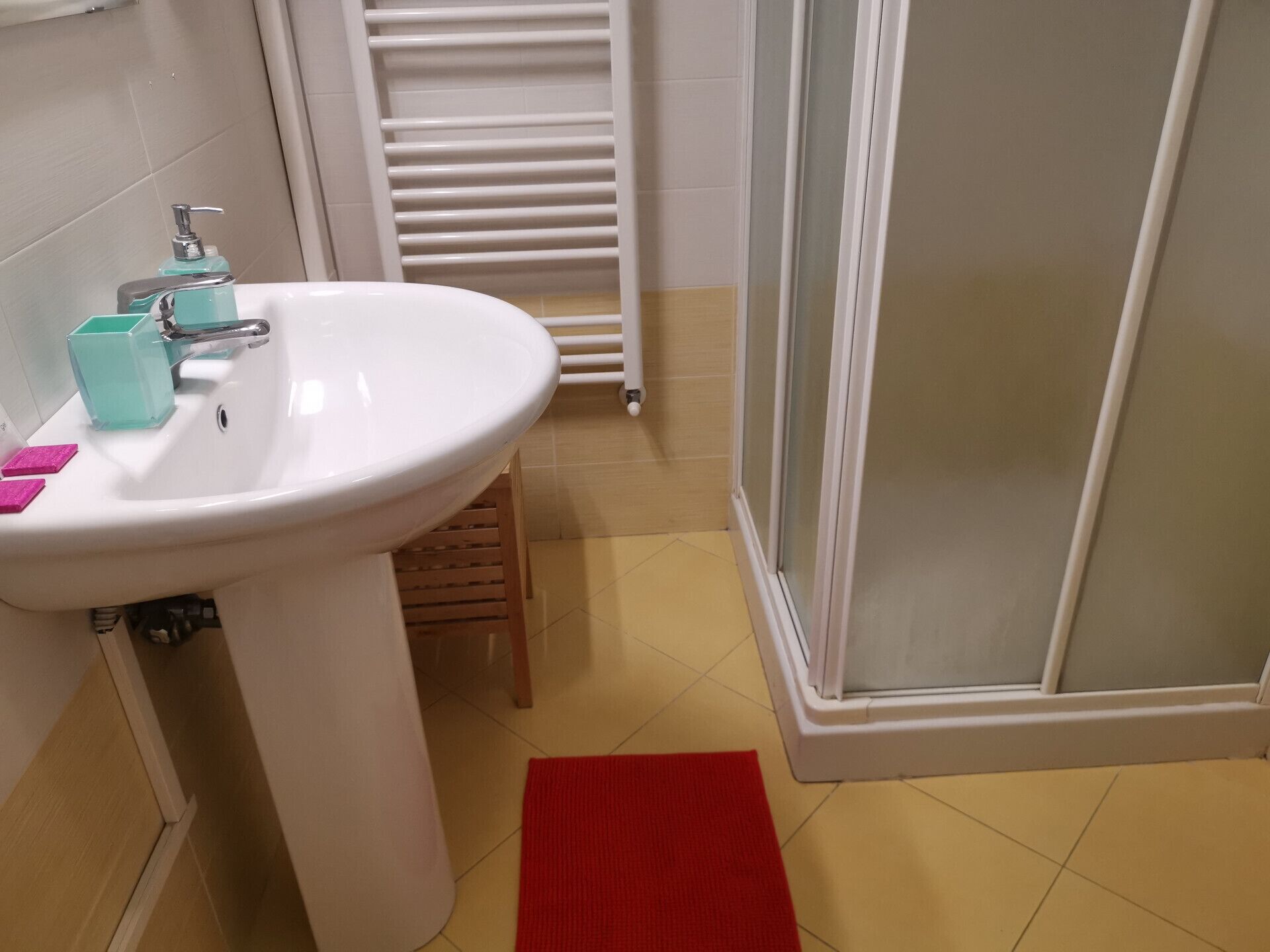 A bathroom with a white sink, a shower with a glass door, and a red mat on the floor.