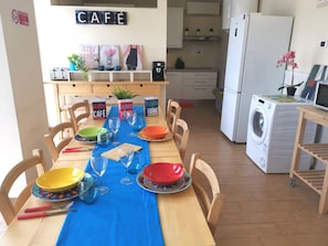 A dining area with a blue tablecloth, wooden chairs, and a kitchen in the background.