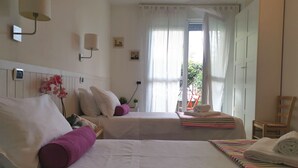 A hotel room with two beds, a window with sheer curtains, a wall-mounted lamp, and a small potted plant.