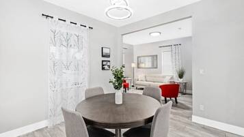 Un espace repas moderne avec une table ronde, des chaises grises et un vase blanc orné d’une plante.