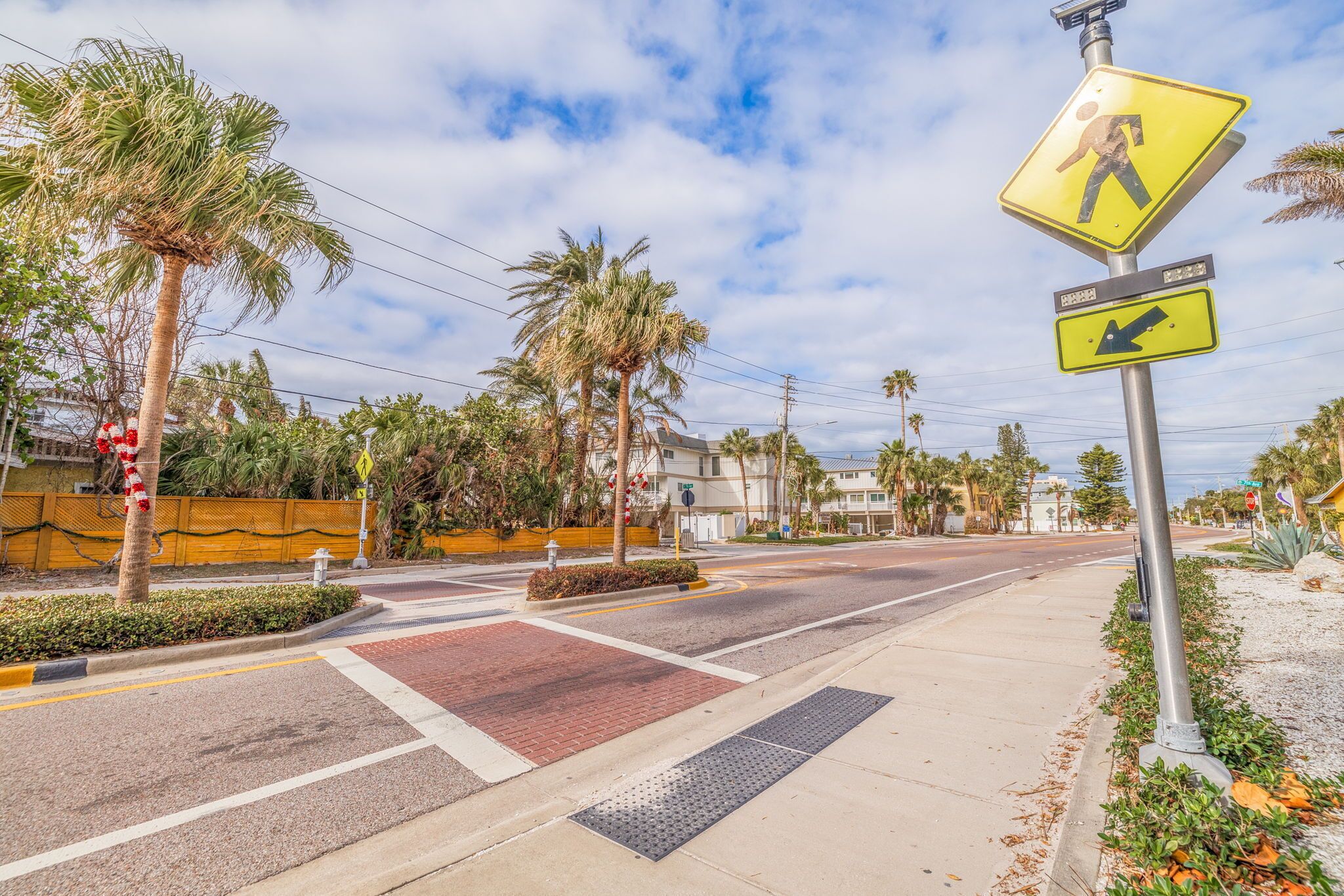 A street with pedestrian crossing signs, palm trees, and a sidewalk.