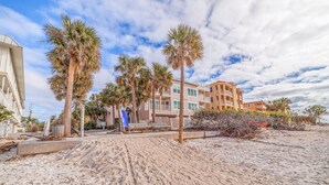 Un hôtel situé en bord de mer, avec des palmiers, une plage de sable fin et un ciel dégagé.
