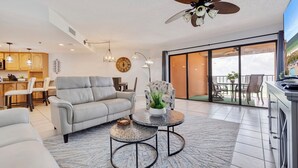 Un salon moderne avec un canapé, deux tables rondes, un ventilateur de plafond et une vue sur le balcon extérieur.
