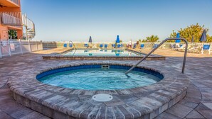 Un bain à remous avec une piscine en arrière-plan, entouré d’une clôture blanche et de chaises bleues.