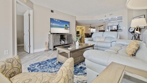Een woonkamer met een televisie, bank, salontafel en vloerkleed.