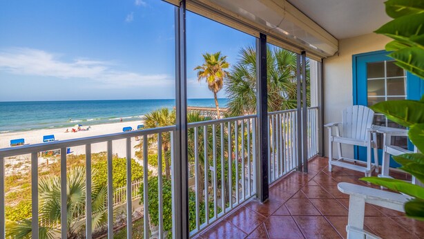 Un balcón con vista a la playa y al océano, que incluye una silla blanca y una mesa.