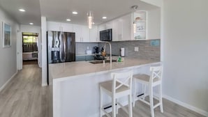Cocina moderna con armarios blancos, una isla grande con taburetes de bar, microondas y refrigerador de acero inoxidable.