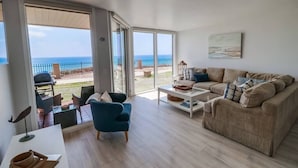 Amplia sala de estar con un gran ventanal corredera que da a un balcón con vistas al mar.