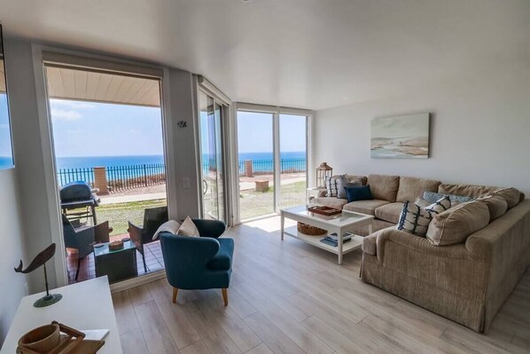 A spacious living room with a large sliding glass door leading to a balcony with a view of the sea. - Private Beach Access | Oceanfront | Pool & Spa (Solana Beach)
