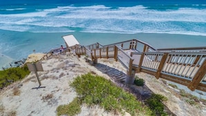 Una escalera de madera baja a una playa con vistas al océano.