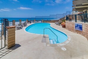 A swimming pool with a view of the ocean, surrounded by lounge chairs and a fence. - Private Beach Access | Oceanfront | Pool & Spa (Solana Beach)