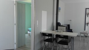 A small, modern room with a desk and two chairs, a bed in the background, and a door leading to another room. - Léon: New House With Heated Pool and Private ; Handi-accessible (Léon)