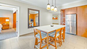 A modern kitchen with a white table, wooden chairs, and a stainless steel refrigerator.