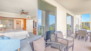 A hotel room with a balcony, a bed, a desk, and a seating area with wicker furniture.