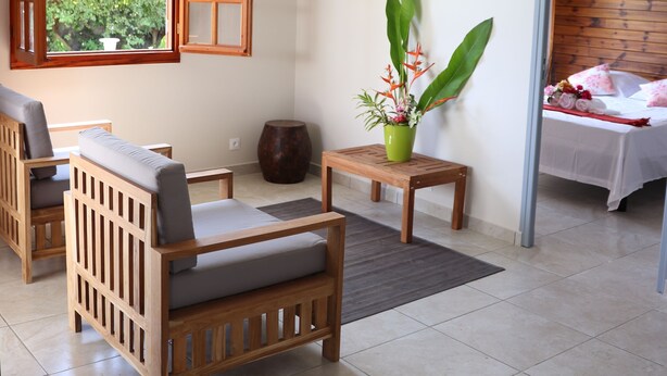 Une pièce comprenant un canapé en bois, une petite table, une plante en pot et un lit avec une tête de lit en bois.