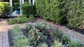 A garden with a wooden deck, various plants, and a pergola structure. - Pristine Southampton Home (Water Mill)