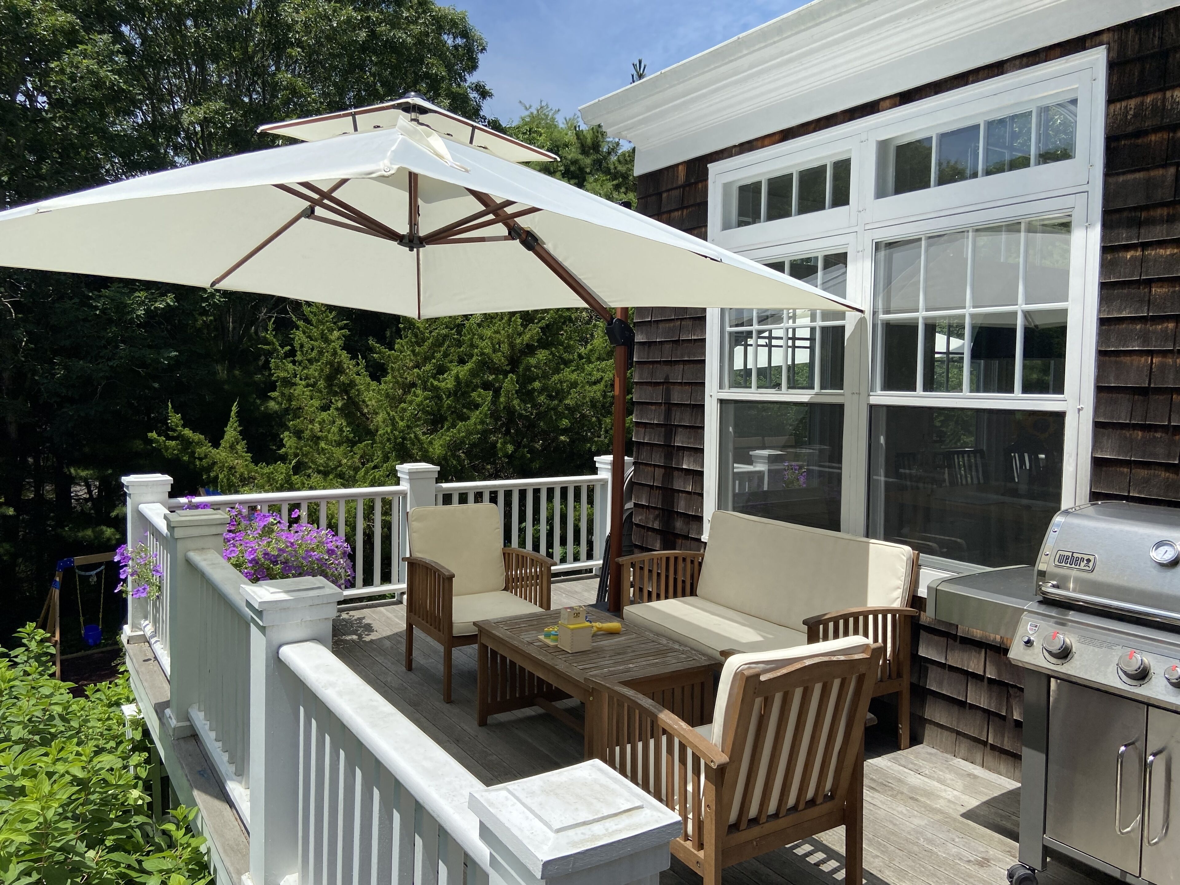 Une terrasse extérieure avec une table et des chaises, un barbecue et un parasol blanc.