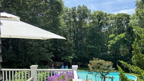 A wooden deck with a white umbrella, a wooden chair, and a potted purple flower. - Pristine Southampton Home (Water Mill)