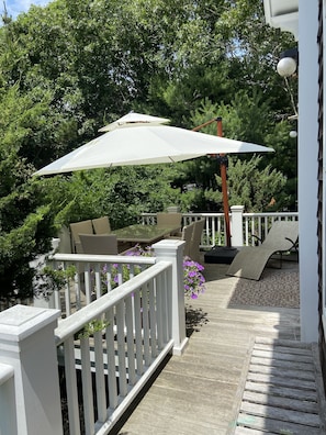 Um deck de madeira com guarda-corpos brancos, móveis de exterior e uma pérgola com guarda-sol branco.