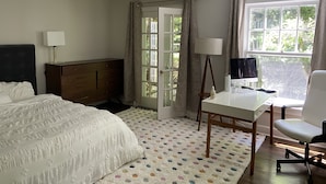 A bedroom with a bed, a desk, a chair, a lamp, a dresser, and a window with curtains. - Pristine Southampton Home (Water Mill)
