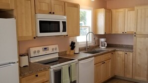 A kitchen with wooden cabinets, a microwave, a stove, a sink, and a coffee maker.