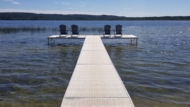 A wooden dock extending into a calm lake with clear water, surrounded by forested hills.
