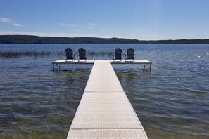 A wooden dock extending into a calm lake with clear water, surrounded by forested hills. - Lakeside Cottage #2, Waterfront on Upper Herring Lake, AC, Kayaks, SUPs, Rowboat (Frankfort)
