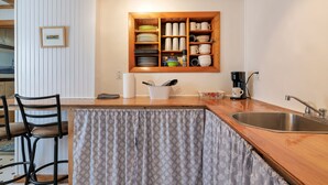 A kitchen with a built-in shelf unit holding dishes and cups, a wooden countertop, and a sink.