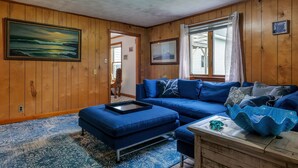 A room with wooden paneling, a blue sofa, a tray table, and a decorative bowl on a wooden table.