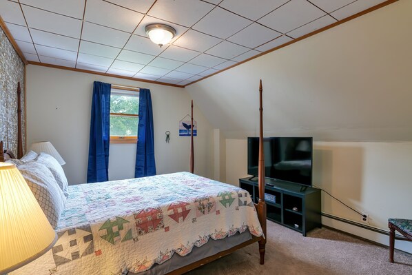 A bedroom with a four-poster bed, a television, and a window with blue curtains.