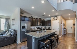 A modern kitchen with dark cabinets, a granite island, and a built-in oven.