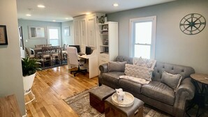 A spacious living room with a grey sofa, wooden flooring, and a dining area with a table and chairs. - BRADLEY BEACH HOUSE with Private Backyard  (Bradley Beach)