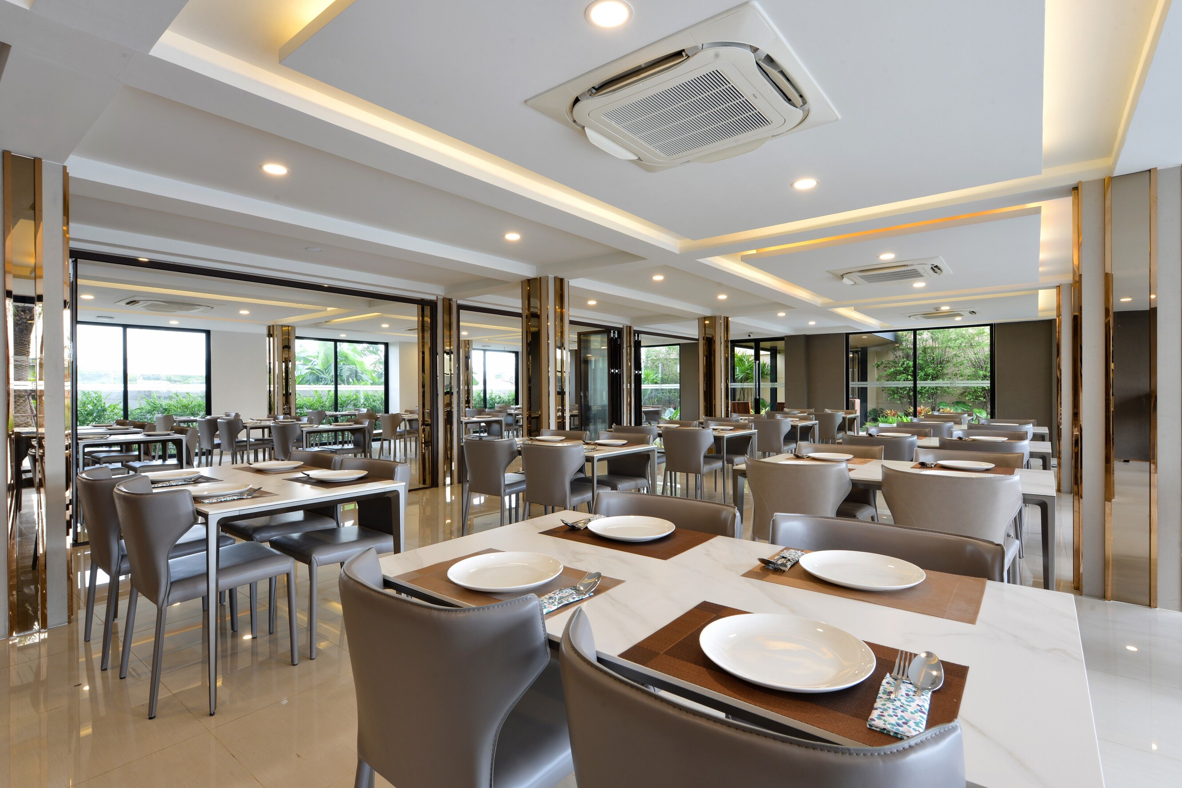 A modern dining area with tables set for four, large windows, and a high ceiling with recessed lighting.