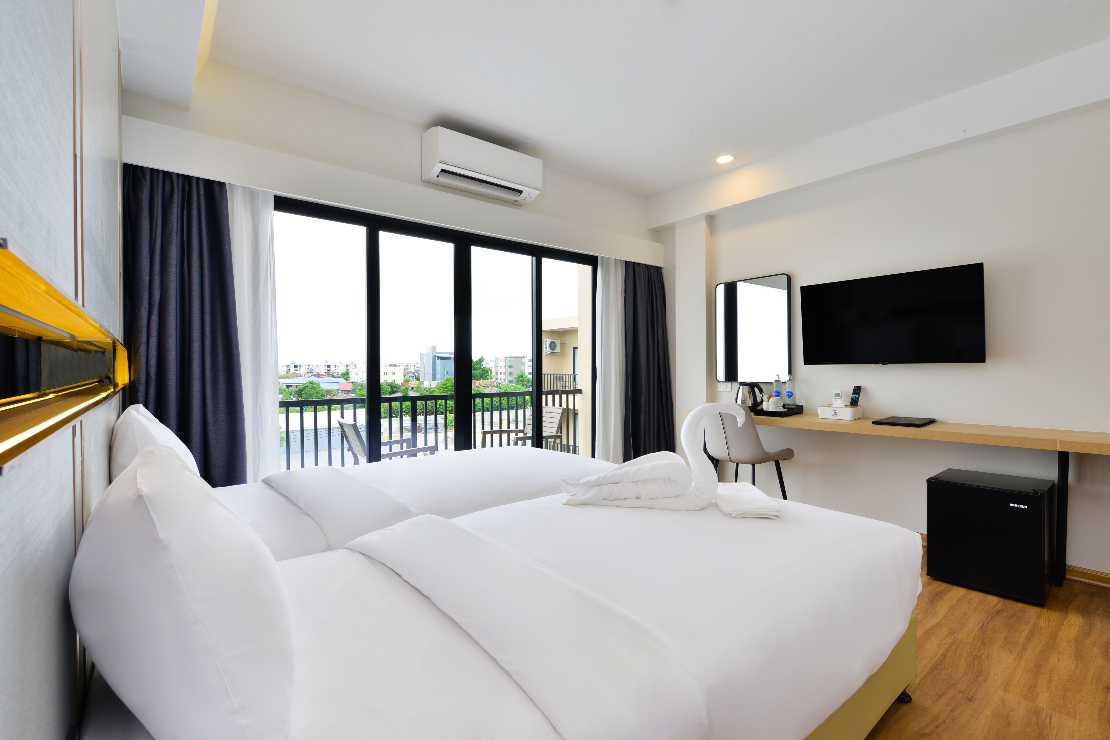 A hotel room with a large bed, a desk with a computer, a TV, and a view of the city.