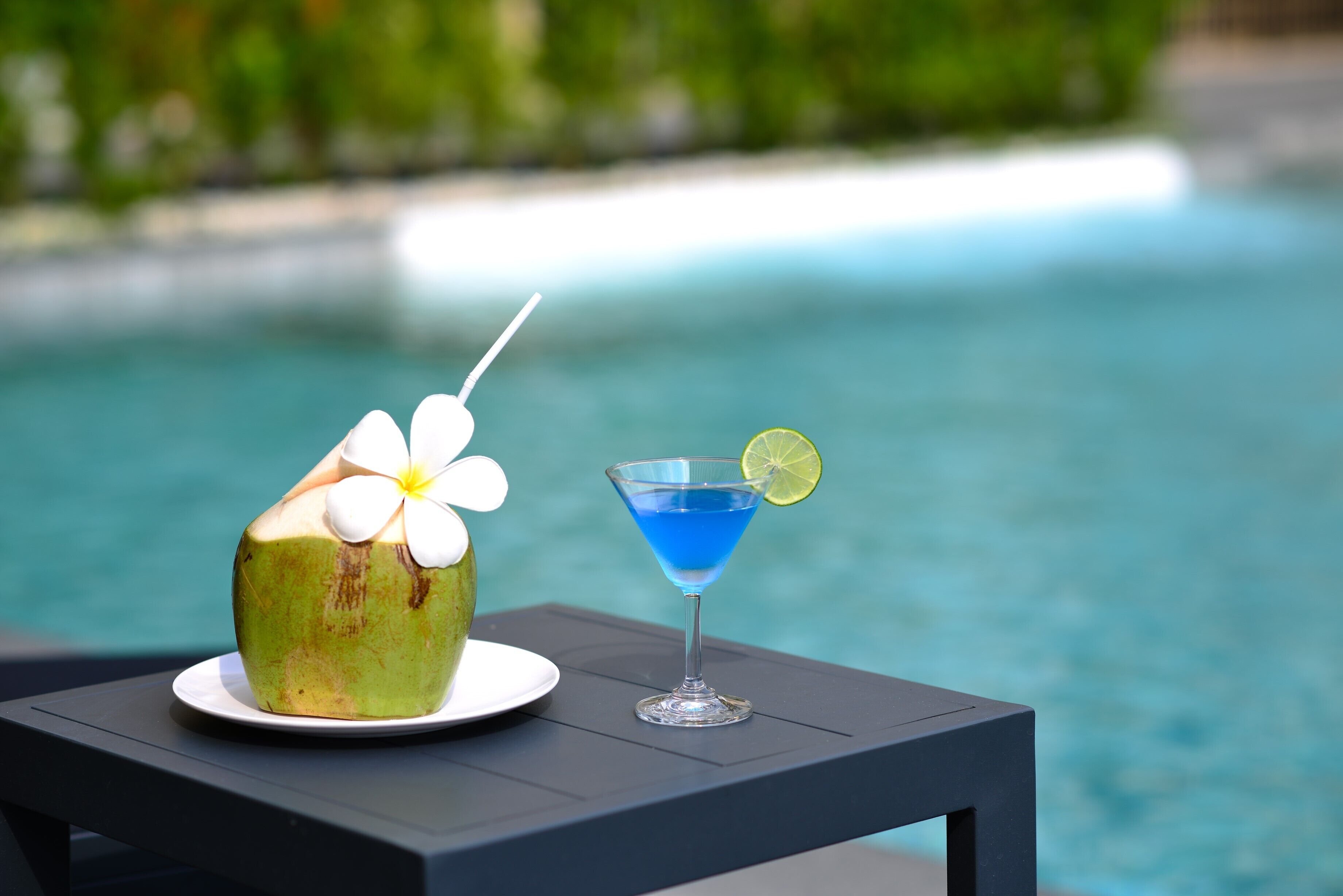 Una mesa con un refresco de coco y un cóctel junto a la piscina.