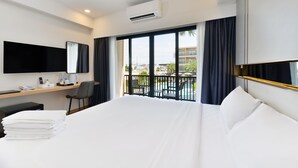 A hotel room with a large bed, a desk with a chair, a flat-screen TV, and a balcony with a pool view. - Grand BS Airport Hotel Suvarnabhumi (Bangkok)