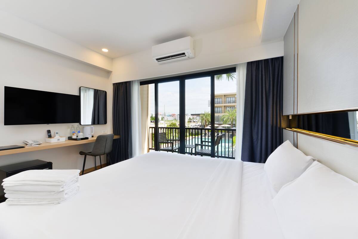 Ein Hotelzimmer mit einem großen Bett, einem Schreibtisch mit Stuhl, einem Flachbildfernseher und einem Balkon mit Blick auf den Pool.