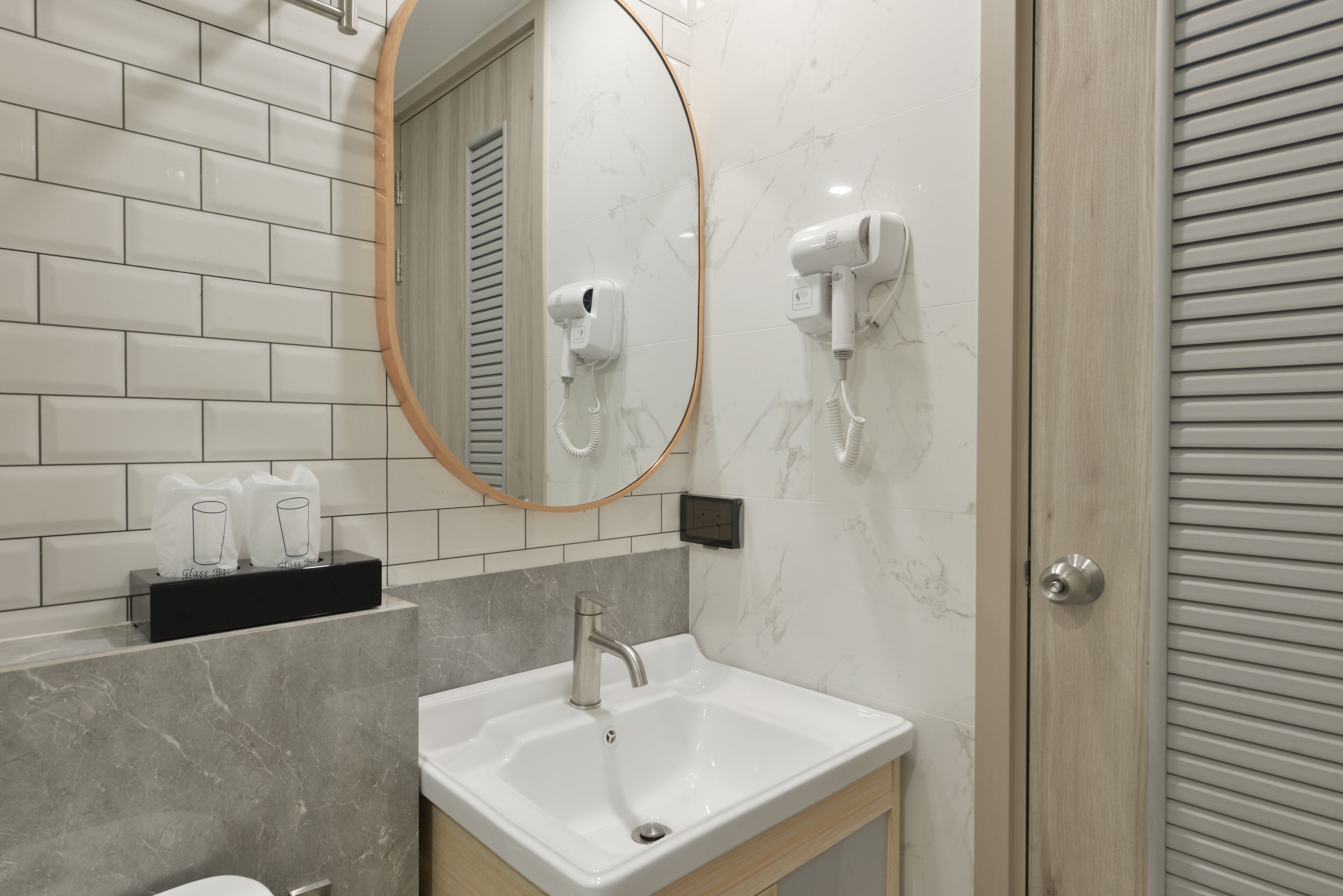 A modern bathroom with a white sink, a mirror, and two hair dryers mounted on the wall.