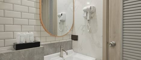 A modern bathroom with a white sink, a mirror, and two hair dryers mounted on the wall.