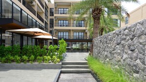 A modern building with a stone wall and a pathway leading to a covered area with umbrellas. - Grand BS Airport Hotel Suvarnabhumi (Bangkok)