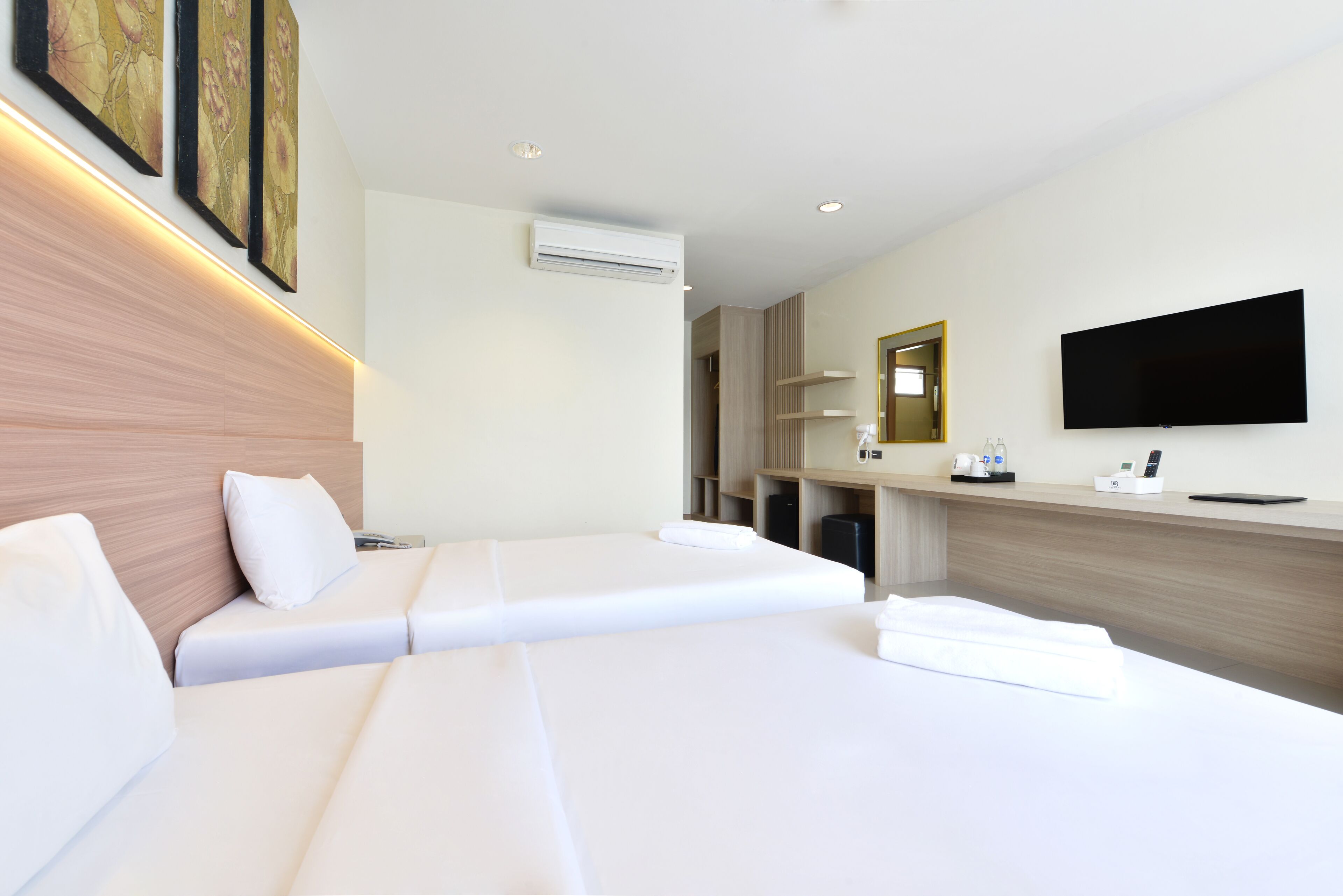 A hotel room with two beds, a flat-screen TV, a mirror, and a wooden headboard.